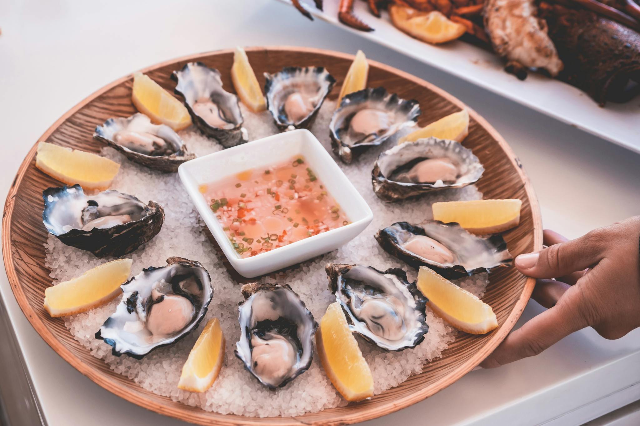 Anonymous person serving plate of fresh oysters with sauce and lemons on table